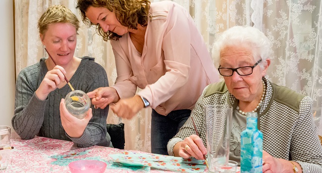 Drie vrouwen zijn creatief bezig met het schilderen van glazen potjes